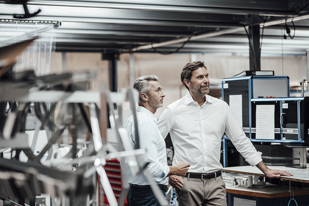 Colleague discussing with smiling manager while standing by manufacturing machinery in factory